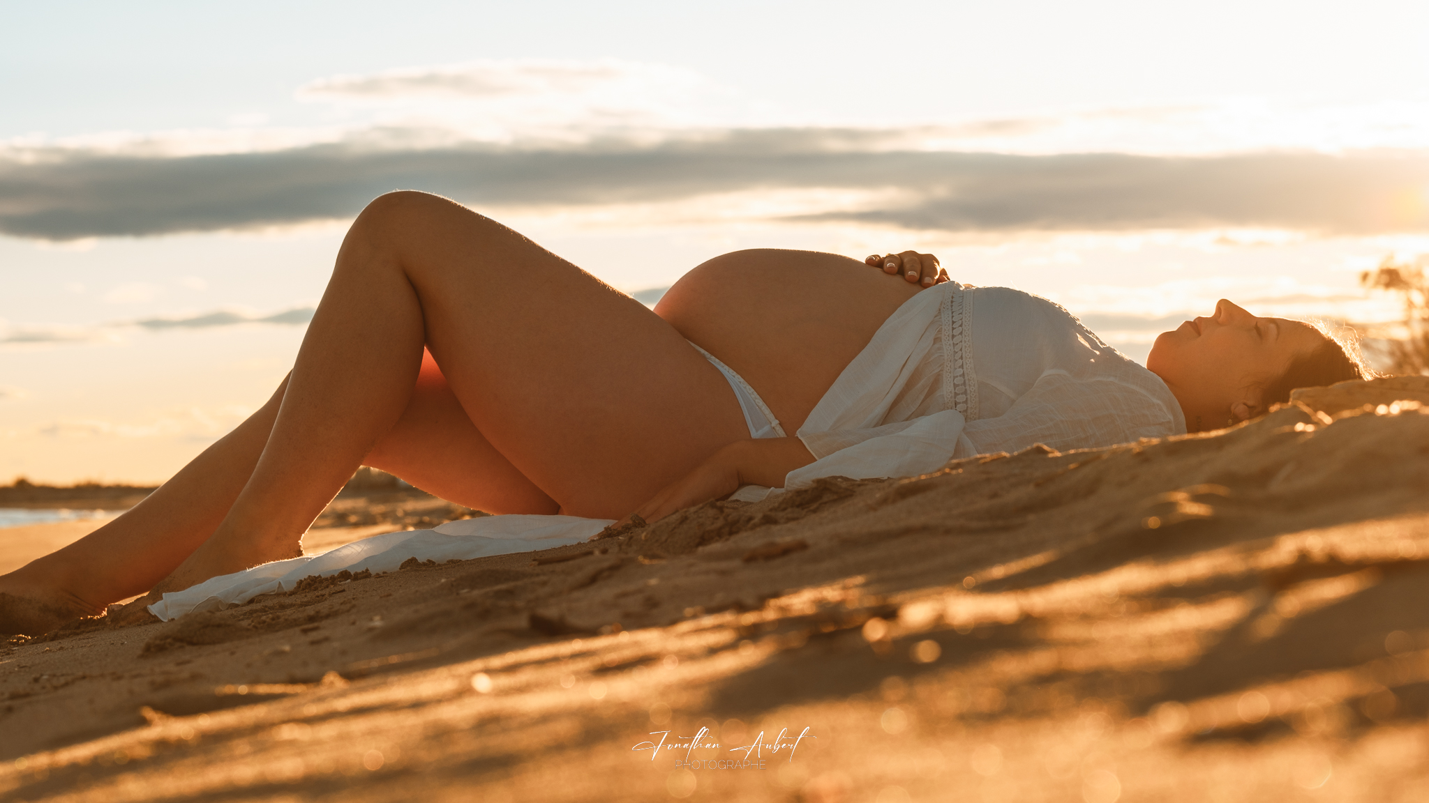 Séance grossesse allongée sur la plage en lumière dorée